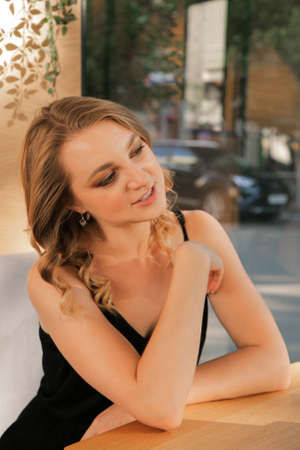 A young businesswoman communicates with someone sitting at a table, behind the glass of the street