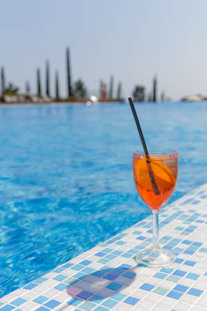 Orange cocktail with a straw on the background of the pool with clear blue water, in the background...