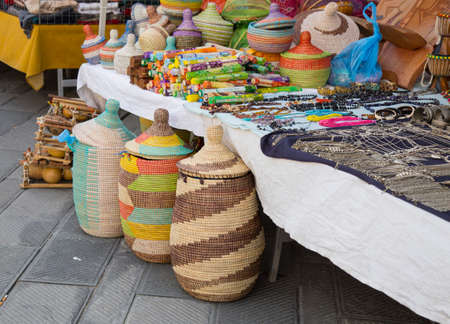Assorted colorful handcrafted woven baskets on a street market stall with jewellery alongside viewed closeupのeditorial素材