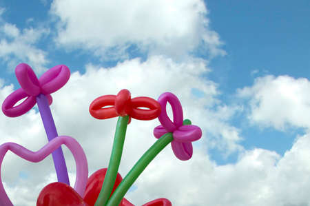 Colorful decorative party balloons tied into flower and heart shapes viewed low angle against a blue sky with white clouds and copy spaceの写真素材