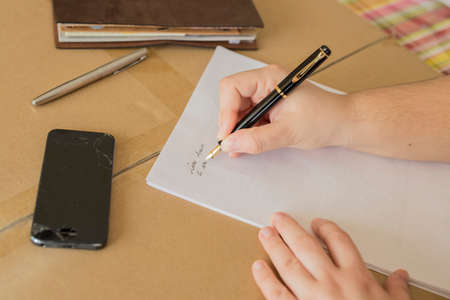 horizontal cross-hair image of a hand writing a letter with broken phone on the deskの写真素材