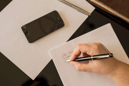 horizontal cross-hair image of a hand writing a letter with broken phone on the deskの写真素材