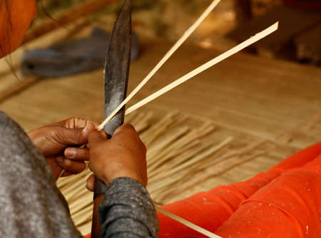 woman cutting strips of bamboo with a steel knife in her hut preparing to use them. Northern...
