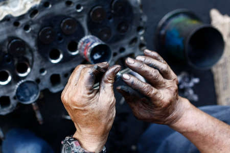 dirty, greasy Asian man's hands, oiling and greasing valves and pistons and inserting into an engine block in a dirty workshop in Thailand, Southeast Asiaの写真素材
