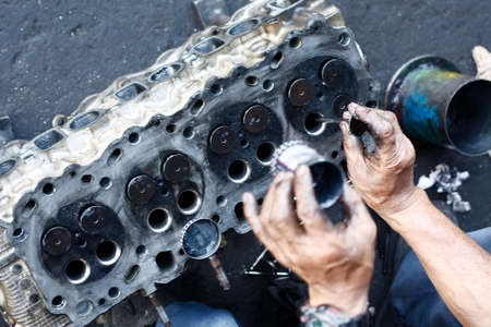 dirty, greasy Asian man's hands, oiling and greasing valves and pistons and inserting into an engine block in a dirty workshop in Thailand, Southeast Asiaの写真素材
