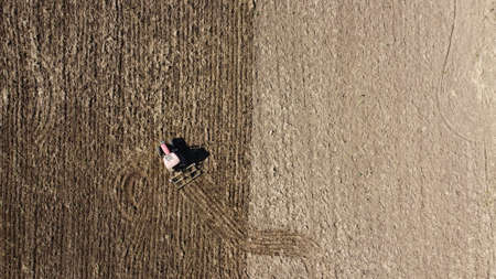 top down drone view of an old red tractor tilling a large field in preparation for planting a crop...