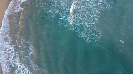 Surfers in the surf waiting for waves in the turquoise ocean off the Victorian Coastline, top down aerial drone viewの写真素材