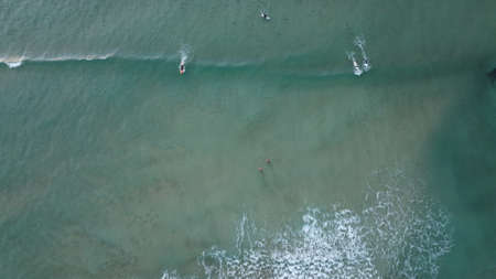 a surfer surfing a turquoise wave into shore at sunsrise along coastal Victoria, top down drone image of multiple surfers in the oceanの写真素材