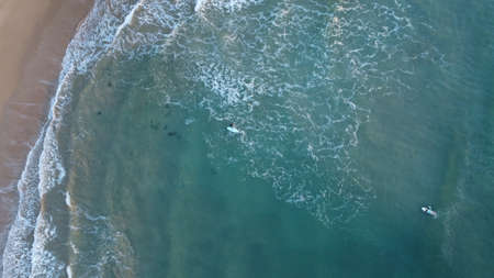 a surfer surfing a turquoise wave into shore at sunsrise along coastal Victoria, top down drone image of multiple surfers in the oceanの写真素材