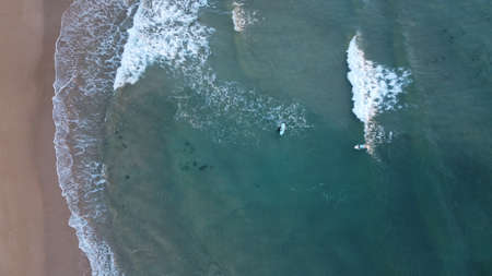 a surfer surfing a turquoise wave into shore at sunsrise along coastal Victoria, top down drone image of multiple surfers in the oceanの写真素材
