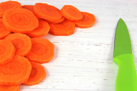 Slices of vivid orange carrot close up on on a distressed wood chopping board with green knifeの写真素材