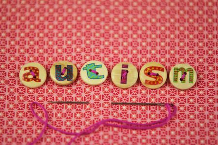 the word autism spelled with buttons with hand painted letters on, on a vibrant textile background.の写真素材