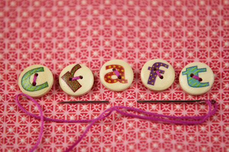 the word craft spelled in hand painted letters on buttons on a vibrant textile background.の写真素材