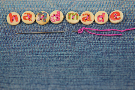 The word handmade spelled in lettered buttons on a denim fabric background with a needle and thread. Word at the top of image with copy space beneath.の写真素材