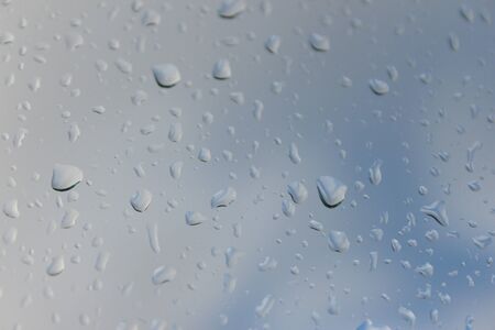 Close up on raindrops on glass window pain, with blue sky and whispy clouds in the background.の写真素材