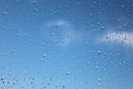 Raindrops on a window pain with a blue sky background.の写真素材
