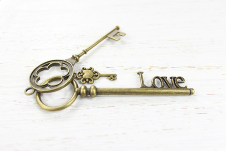 Three brass keys on a white distressed wood background. One key is fashioned with the word Love.の写真素材
