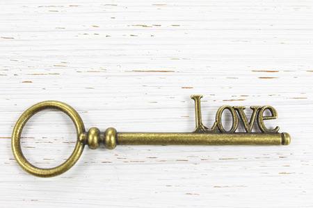 The key to Love. Antique brass key with the word Love on a white distressed wooden background. Copy space.の写真素材