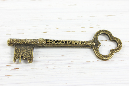 Antique Brass key on a white distressed wood background. Engraved with the Biblical scriprture reference Ephesians 6 verse 19 ( Pray also for me, that whenever I speak, words may be given me so that I will fearlessly make known the mystery of the gospel).の写真素材