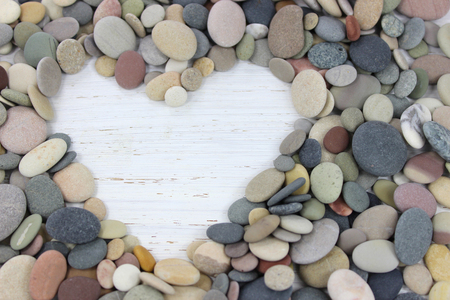 Heart shape made with colorful pebbles on a white distressed wood background.の写真素材