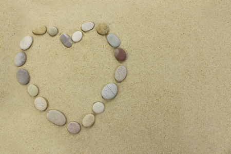 Beach stones in the shape of a heart on a sandy beach background.の写真素材