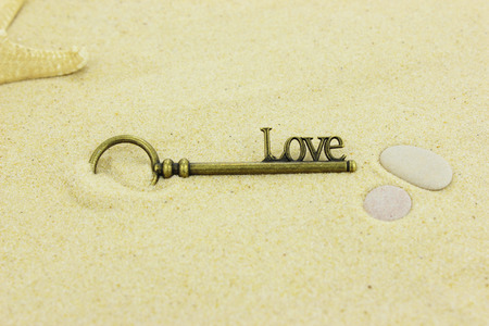 Brass key with the word Love on it lying on a sandy beach.の写真素材