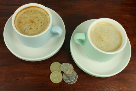 English Coins with two cups of coffee on a dark rustic wooden table.の写真素材