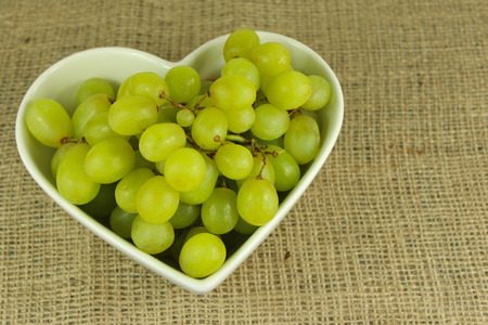 Green grapes in a white heart shaped bowl on a rustic hemp background.の写真素材