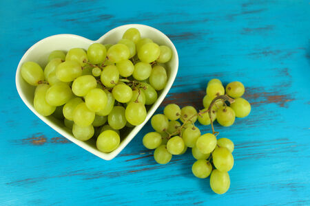 Green grapes in heart shaped bowl on a turquoise distressed wood background. Focus on grapes in bowl.の写真素材