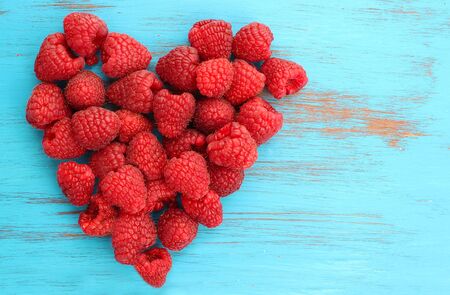 red raspberries in a heart shape on blue wooden backgroundの写真素材