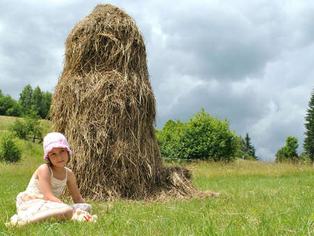 girl sits around stack network on meadow.の写真素材