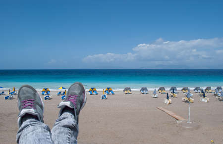 Feet in Sneakers on a background of sea beach with umbrellas.の写真素材