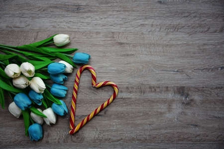 heart made of chocolates and a bouquet of tulips on a wooden backgroundの写真素材