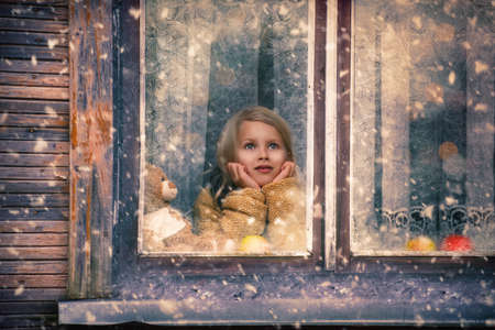 girl looks out the window at the falling snowの写真素材