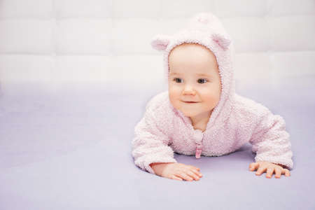 little happy baby in pink suit with ears is lying on his tummyの写真素材