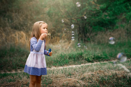 little girl inflates soap bubbles in the summer on the streetの写真素材