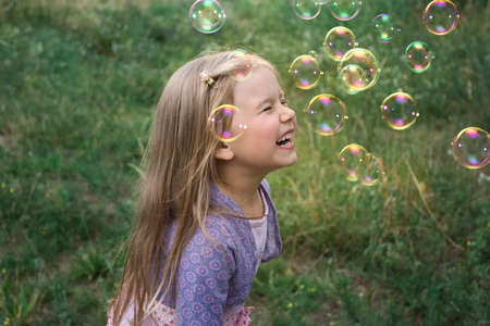 Little girl laughs playing with soap bubbles on the street in summer.の写真素材