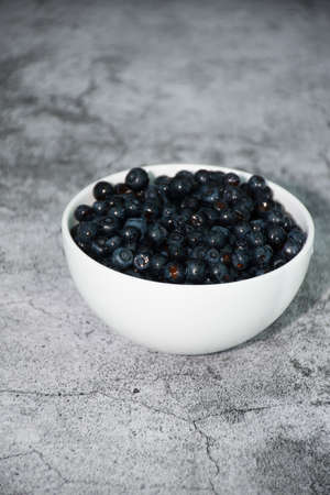 White bowl full of blueberries on gray concrete background