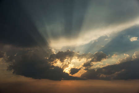 natural dramatic sunset with sunbeams peeping out from behind the cloudsの写真素材