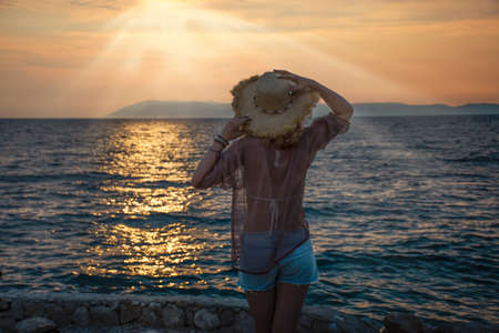 woman in straw hat and shorts by the sea looks at the sunsetの写真素材