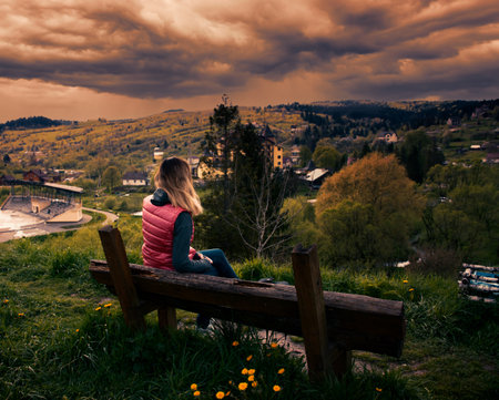 a girl sits on a wooden bench on a mountain and watches the weatherの写真素材