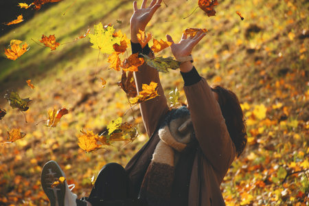 A 50-year-old woman shields herself from falling leaves with her hands, plays with leaves in autumn...