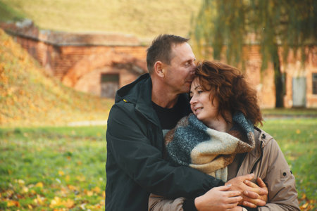 happy married couple over 50 years old, walking in the park in autumn on a warm sunny day, hugging, spending a day off together.の写真素材