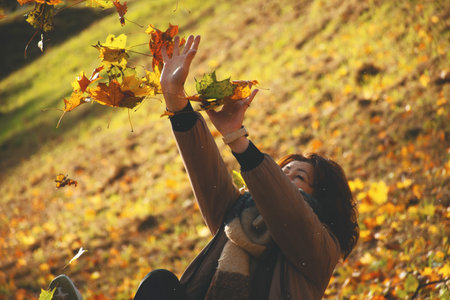 A 50-year-old woman shields herself from falling leaves with her hands, plays with leaves in autumn...