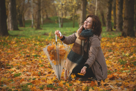 a 50-year-old woman walks in the park in autumn, collects falling leaves in an umbrella and laughs
