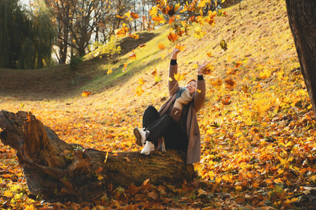 A 50-year-old woman catches falling leaves with her hands, plays with leaves in the fall in the...