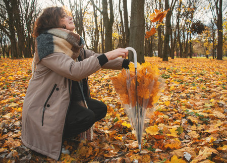 a 50-year-old woman walks in the park in autumn on a warm sunny day, looks at the falling leaves and laughsの写真素材