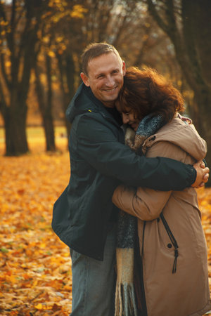 happy married couple over 50 years old, walking in the park in autumn on a warm sunny day, hugging, spending a day off together.の写真素材