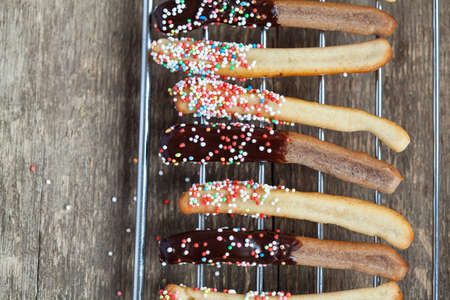 sweet bread sticks with chocolate and colorful sprinkles on a wire mesh rack for children party, selective focus and place for textの写真素材