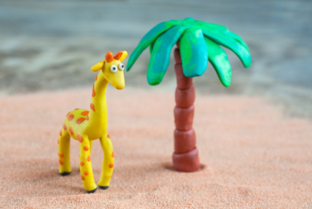 Plasticine world - little homemade yellow giraffe with orange spots and palm on a wooden background, selective focus and place for textの写真素材